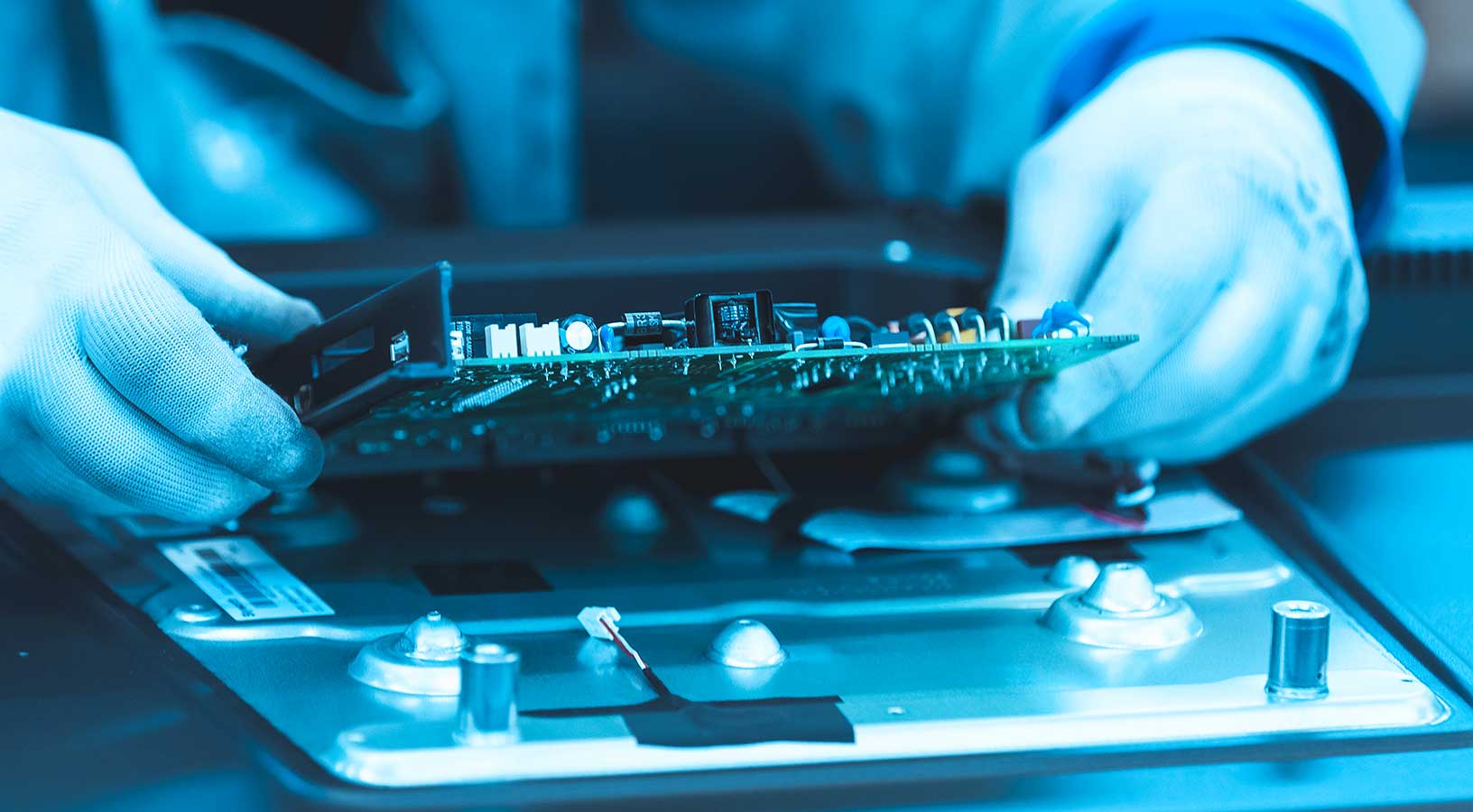Ein Arbeiter mit Handschuhen in einem Elektronikwerk hält eine elektronische Leiterplatte 