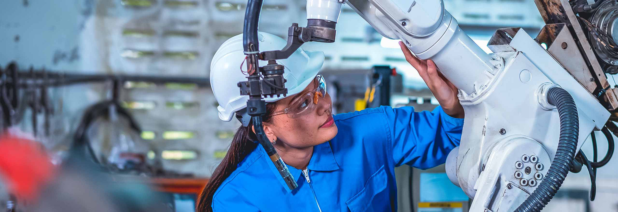 Fabrikarbeiterin hält Tablet und kontrolliert einen Teil einer Robotermaschine im Arbeitsbereich