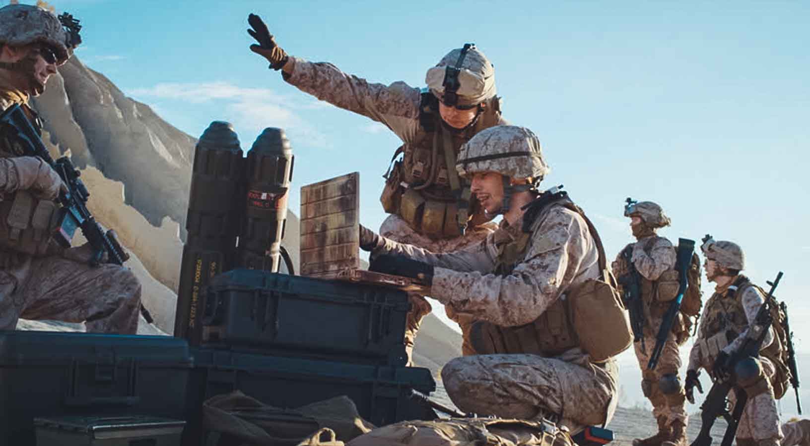 Cinco soldados: dos utilizan un ordenador portátil para vigilar durante una operación militar en el desierto.