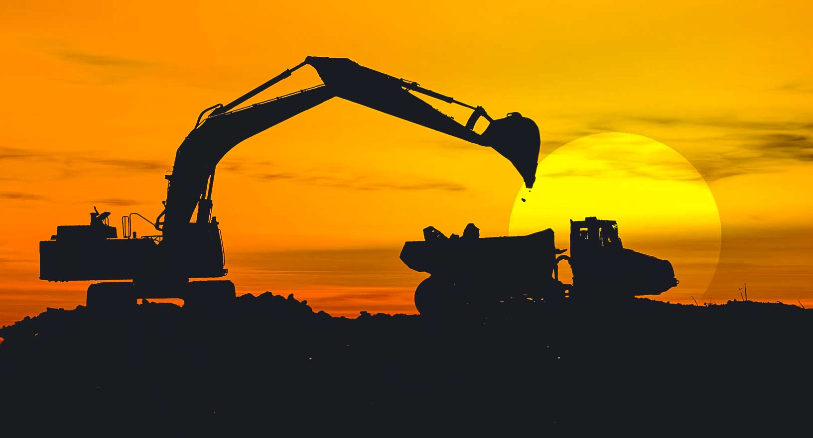 Silhouette eines Baggers, der einen Lastwagen bei Sonnenuntergang auf einer Baustelle füllt 