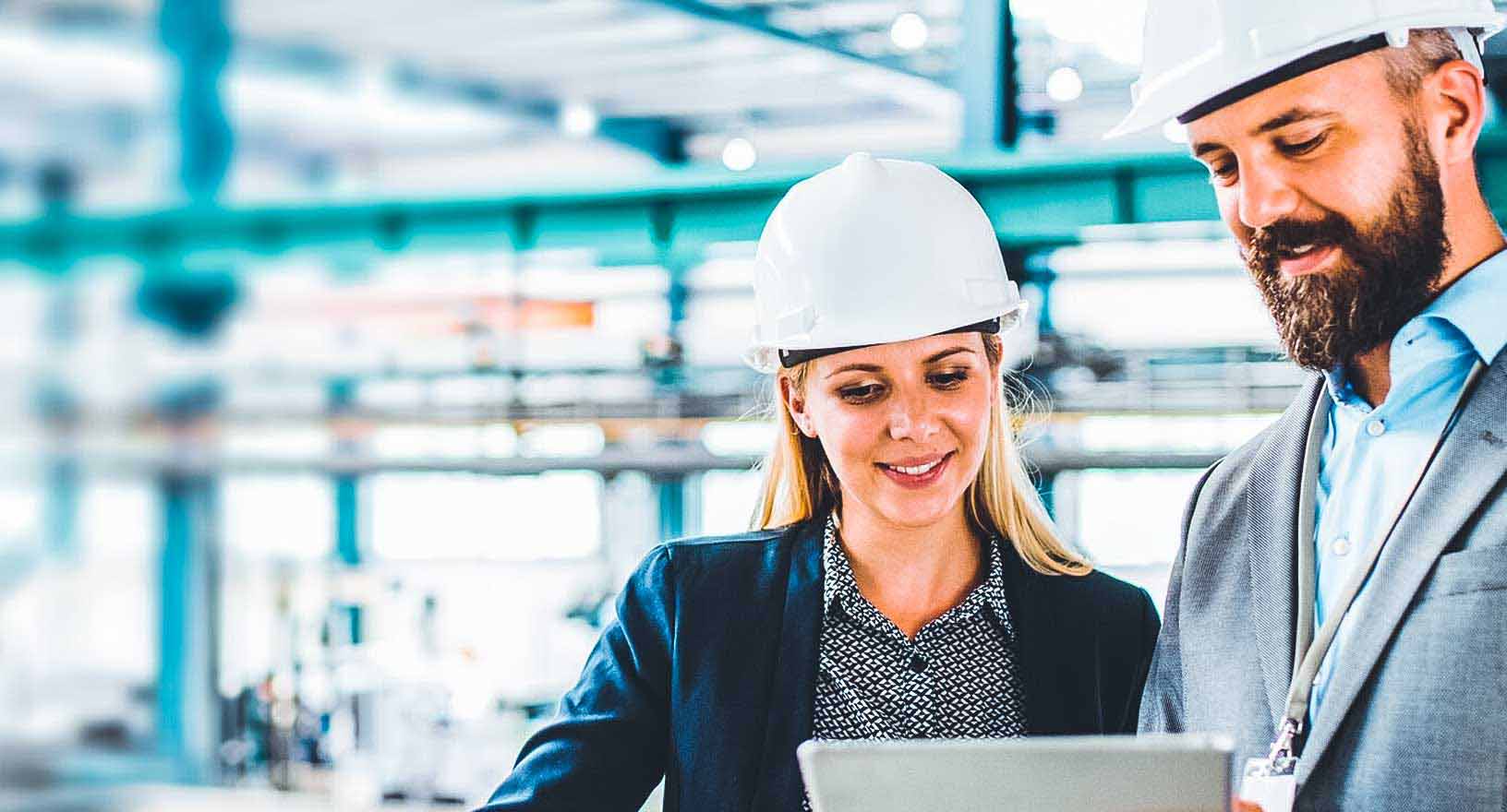 Two colleagues in hard hats review supply management software on a tablet