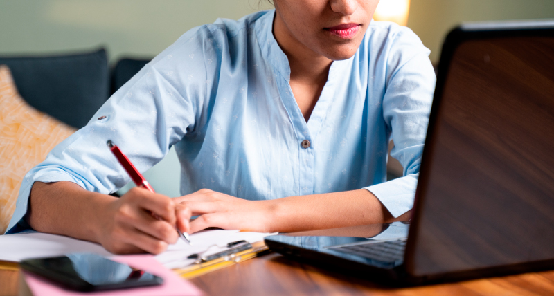 A woman sitting in front of a laptop and writing on a notepad