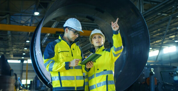 Two plant workers in industrial facility taking notes on mobile device