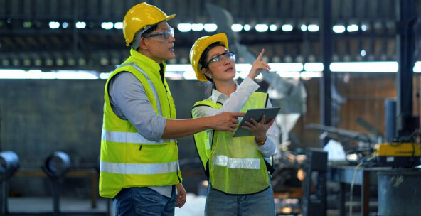 Two plant workers in facility taking notes on tablet while wearing PPE