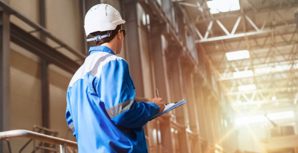 Man in blue jacket writing on clipboard in factory