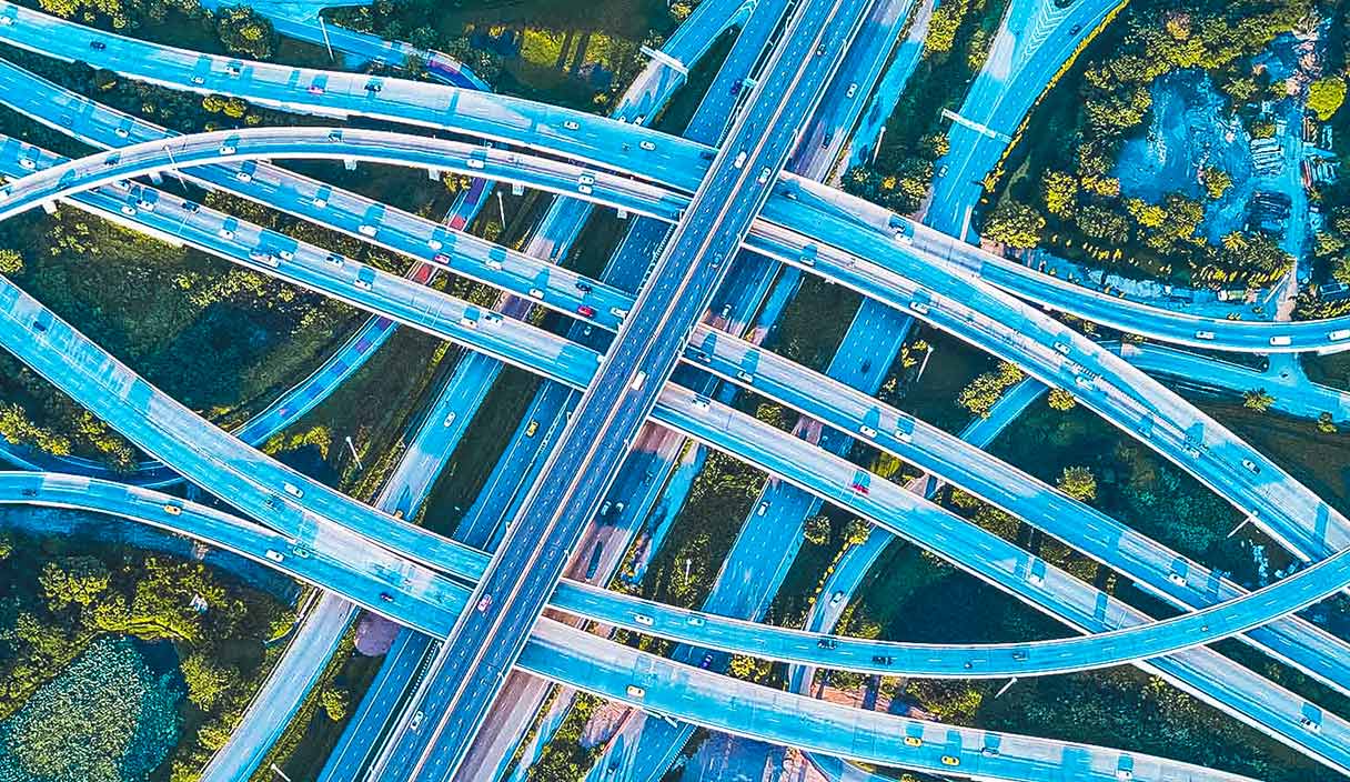 Aerial drone shot of road interchange or highway intersection with busy urban traffic speeding on the road