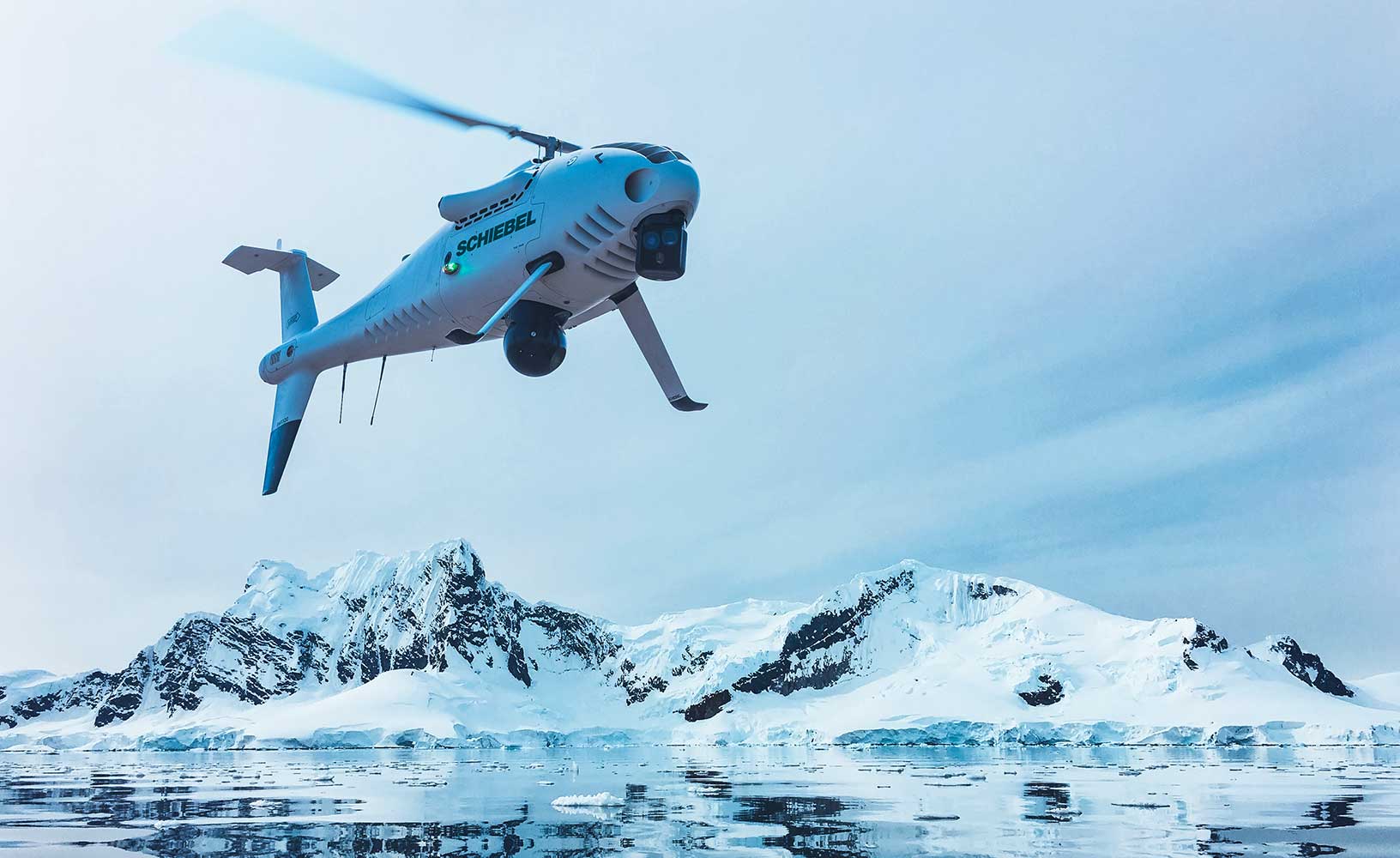 A white Schiebel CAMCOPTER flying above arctic waters.