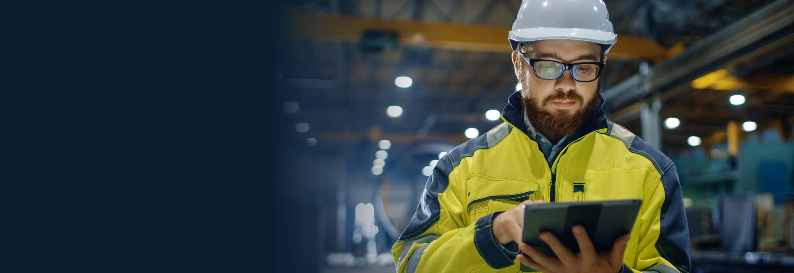 Ingénieur industriel portant un casque de sécurité, un gilet de sécurité et utilisant une tablette tactile.