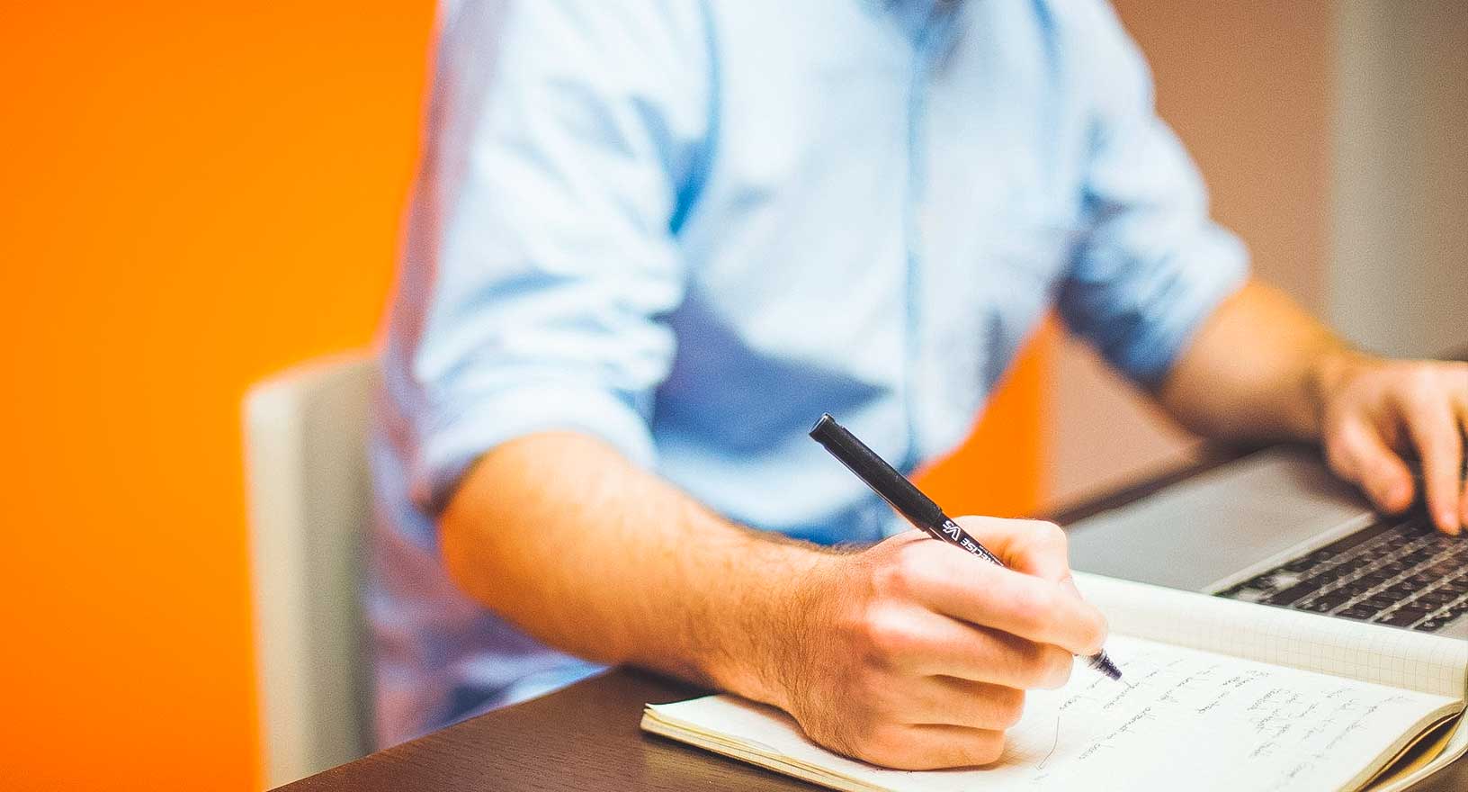 Homem fazendo anotações ao trabalhar no computador em uma sala de conferência