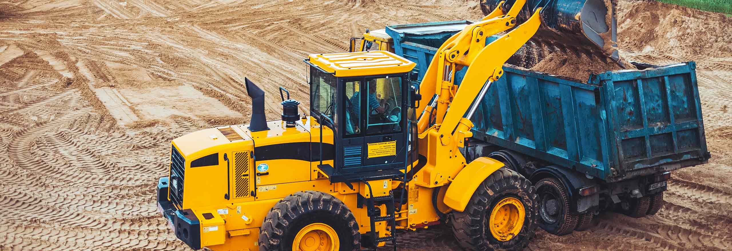 A yellow dozer dumping dirt into a blue dump truck, with four orange and white dump trucks waiting in the background. 