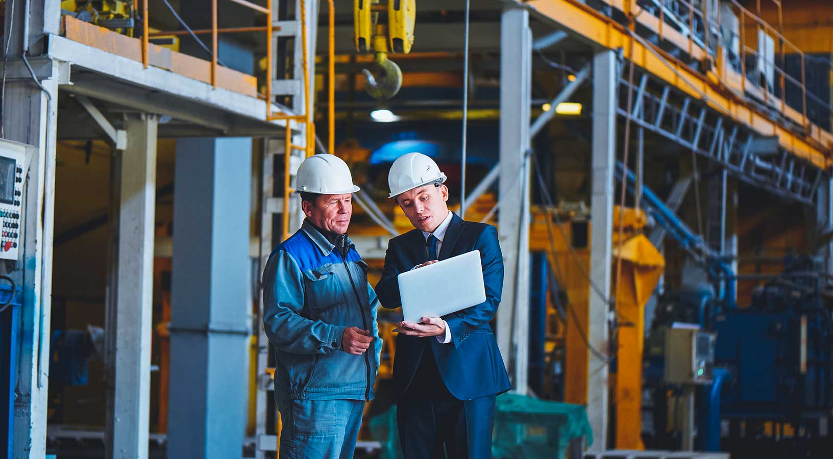 Two men in hard hats discuss project controls at a job site