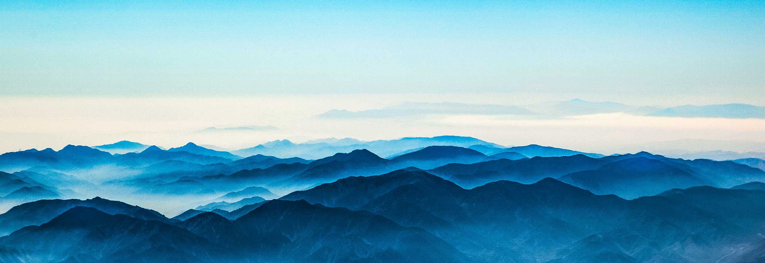 An aerial view of fog lifting from a mountain range.