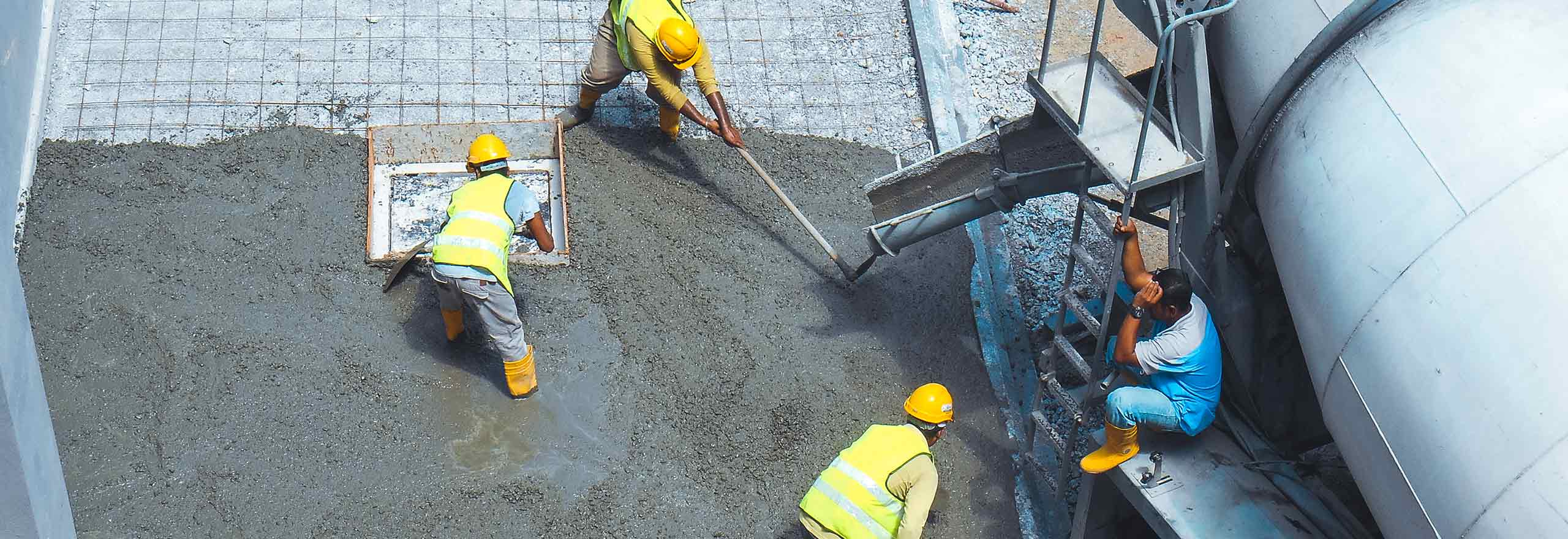 Construction workers using a variety of equipment to pour and smooth a concrete slab section.