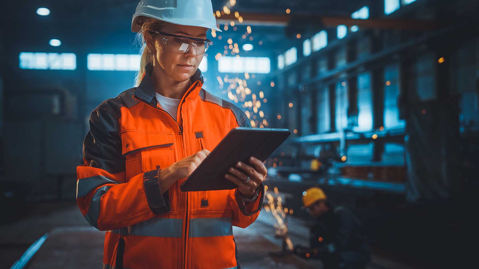 Lavoratore in piedi in uno stabilimento industriale che utilizza un tablet per digitalizzare i flussi di lavoro e le operazioni.