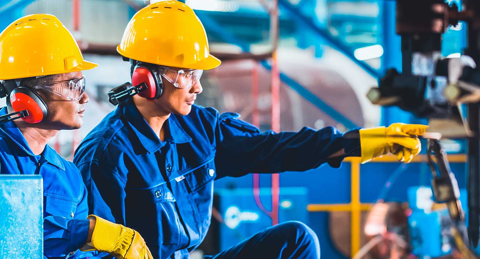 Trabalhadores em ambiente de fabricação, praticando a segurança no local de trabalho com capacetes, proteção auricular e luvas