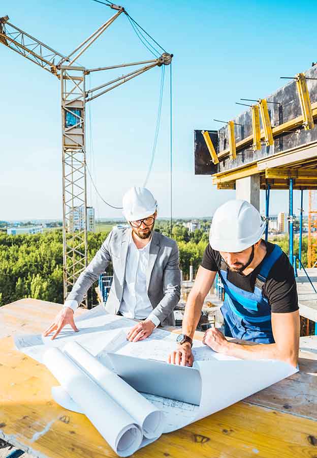 Engineer with worker in uniform working with architectural drawings and laptop at the table on the construction site outdoors