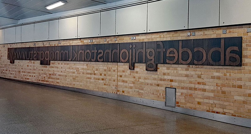 The alphabet made from stained wood in reverse on a brick wall at Farringdon tube station in London