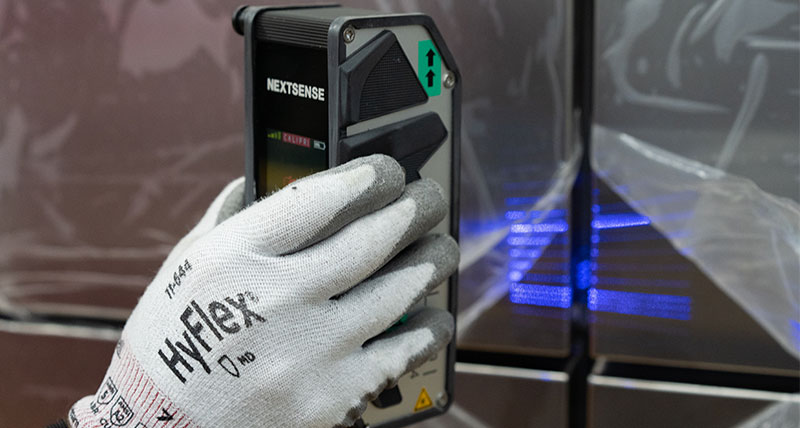A close up of a gloved hand holding a profile and surface measuring device inspecting a gap