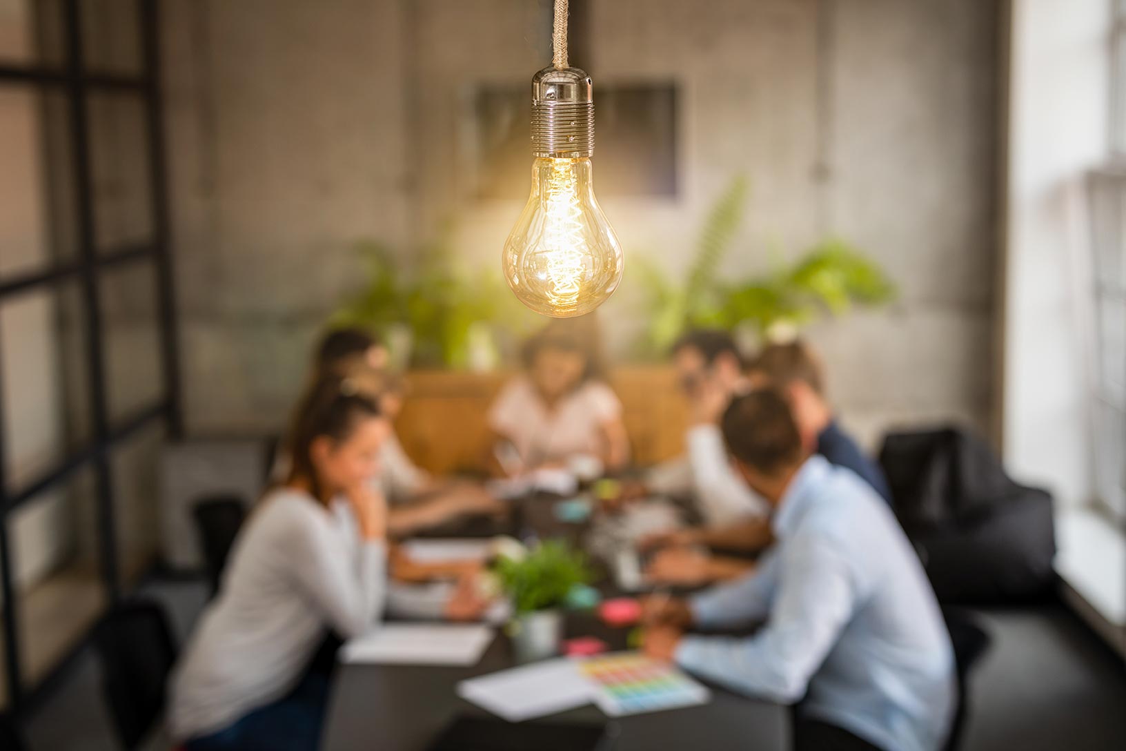 People sitting at a table collaborating with a light bulb hanging above them
