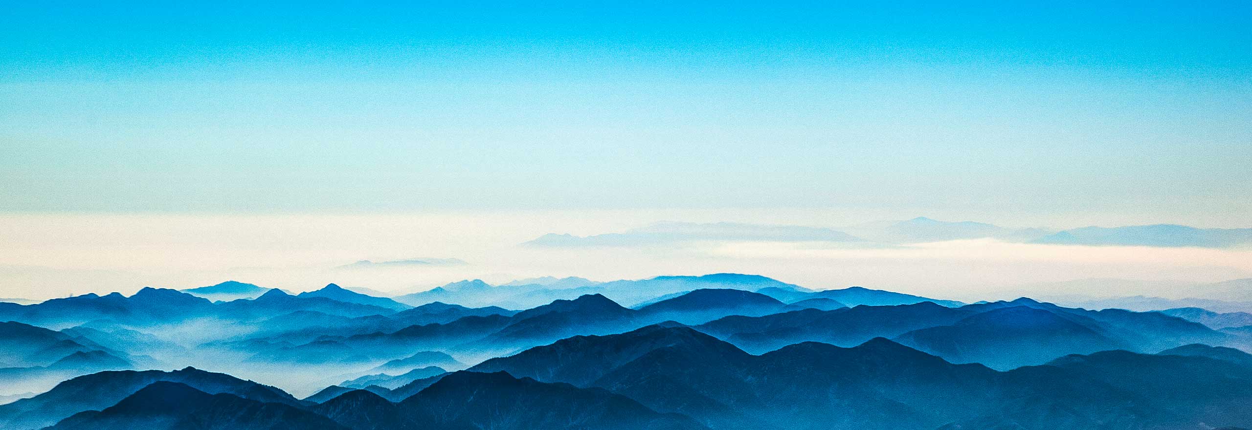 The horizon looks over cloudy mountain tops with the blue sky in view.