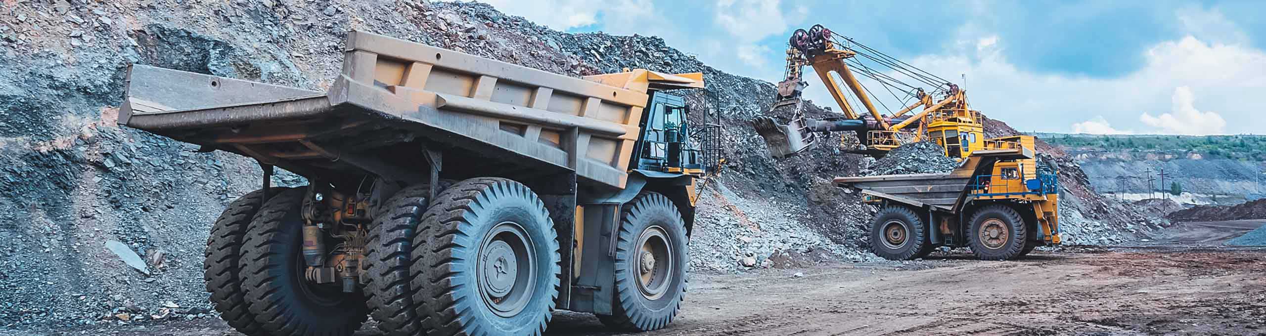 grande escavadeira amarela extraindo minério de ferro em mina a céu aberto e carregando um caminhão pesado