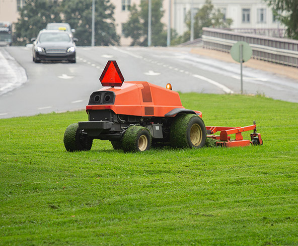 An autonomous mower in a green field near a highway