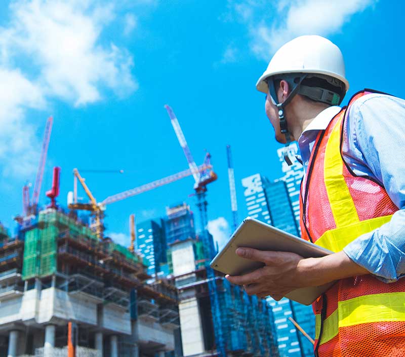 An engineer holding a tablet, gazing upon a building construction project that is maximising the use of its data thanks to the power of construction automation 