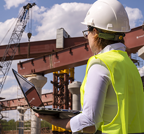 Image of construction professional carrying a laptop through a construction project site