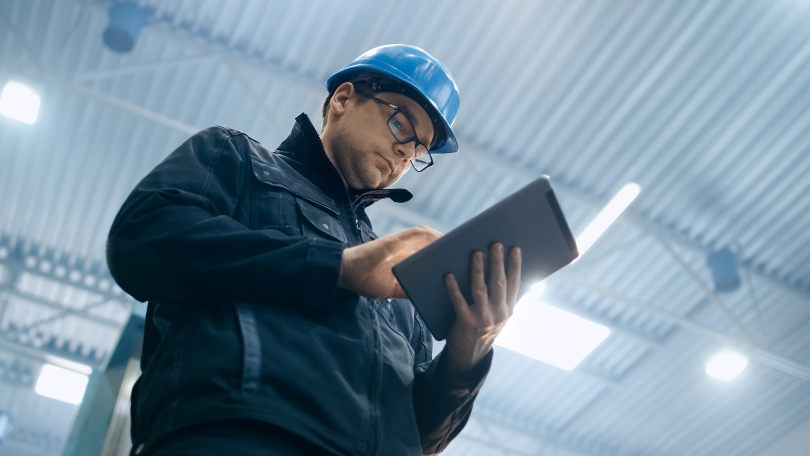 Factory worker in a hard hat is using a tablet computer to access his supplier portal app.