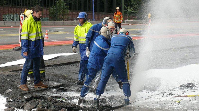 Workers repair a pipeline under a section of pavement