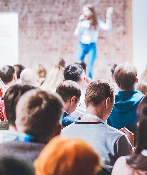 A full audience listens to a guest speaker give a presentation