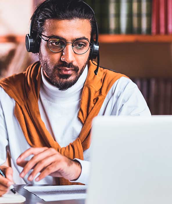  A student in a library watches a video on his laptop with headphones