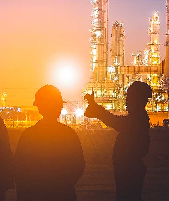 Au coucher du soleil, silhouette d’une équipe d’ingénieurs qui travaille dans une raffinerie de pétrole et de gaz située dans une grande zone industrielle énergétique.