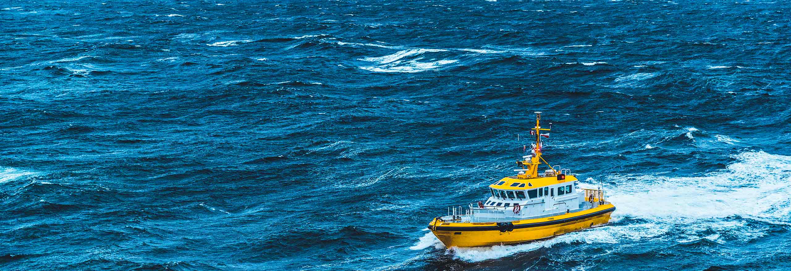 A yellow coast guard vessel is shown offshore in a choppy, stormy sea.