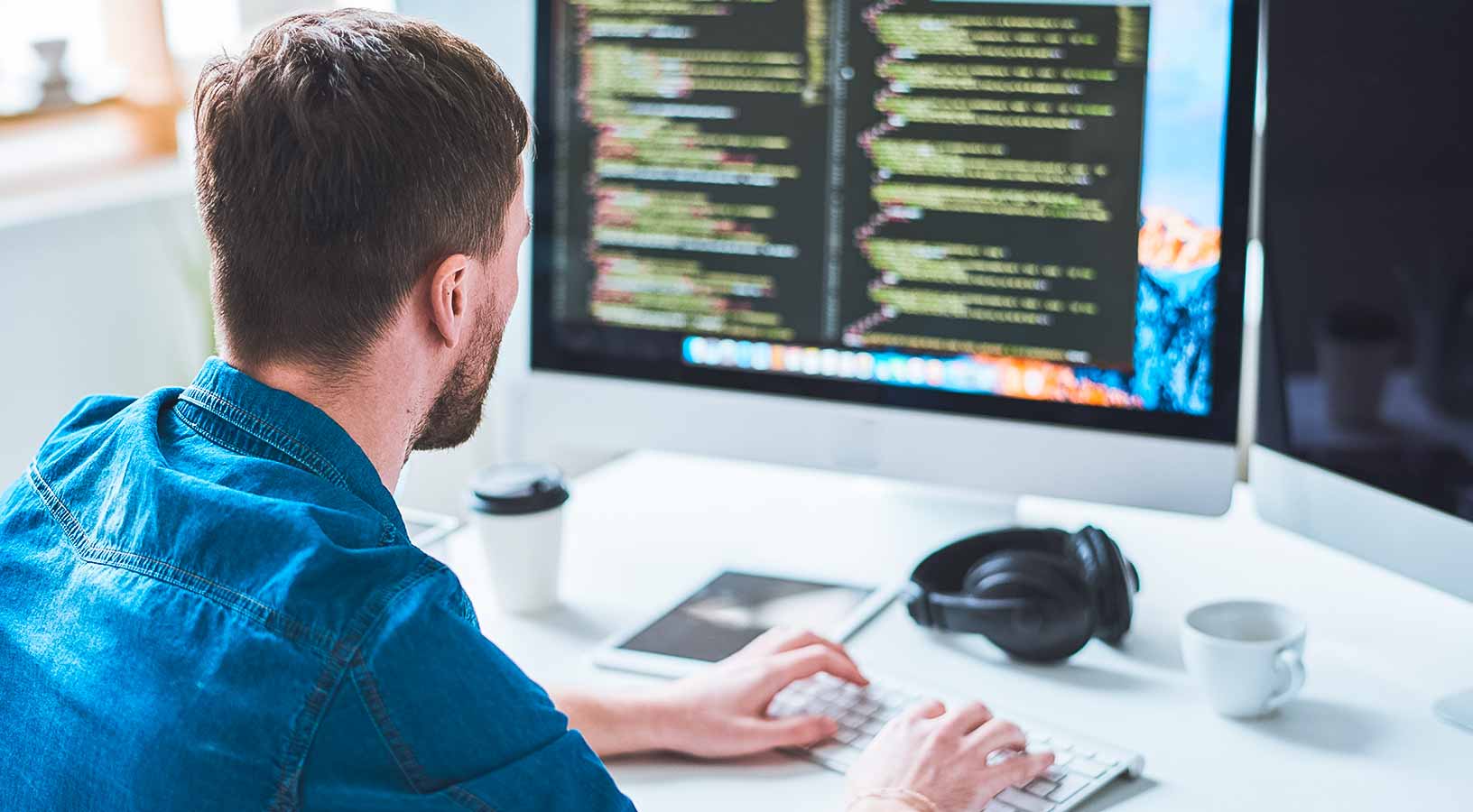 Vista di spalle di un programmatore web impegnato nella scrittura di un codice, seduto alla scrivania e al lavoro su un progetto di startup in un ufficio moderno 