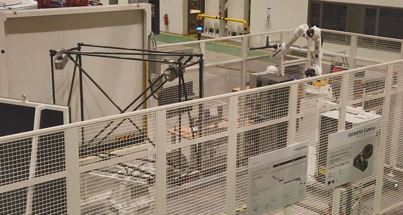 An inspection cell with a white fence around it which contains robotic arms and photogrammetry equipment inspecting wind turbine components