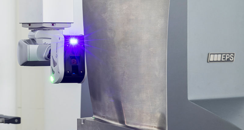 Un scaner laser 3D atașat la o mașină de măsurat în coordonate. Scanerul este poziționat astfel încât laserul cu lumină albastră să fie vizibil