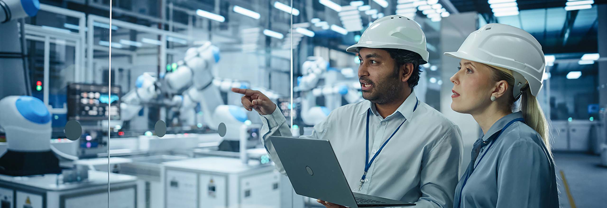 Man and Woman with a laptop looking towards Advanced Manufacturing machines that are in use