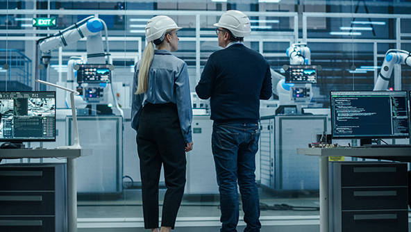 Man and Woman facing Advanced Manufacturing machinery wearing hard hats