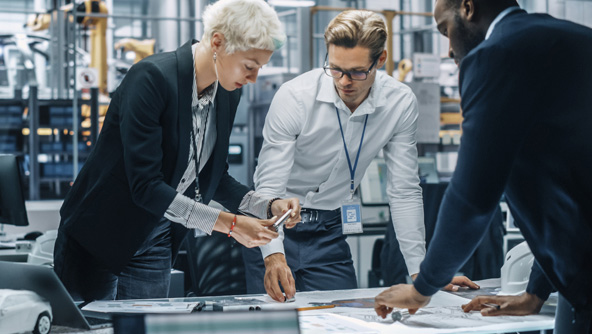 Three people stood over a desk working together in a manufacturing environment