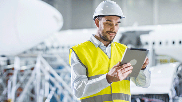 An engineer in an aircraft hangar using a tablet device with aircraft in the background