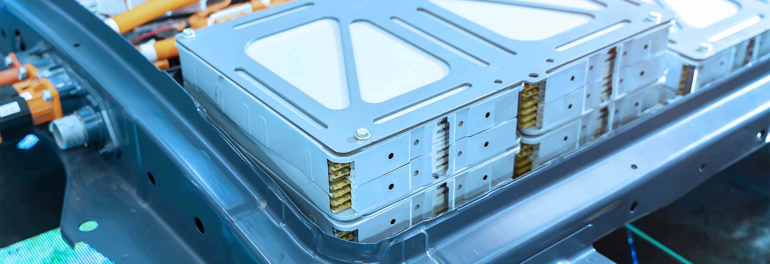An electric vehicle lithium battery pack in blue hues with orange power connections sitting in a car engine bay