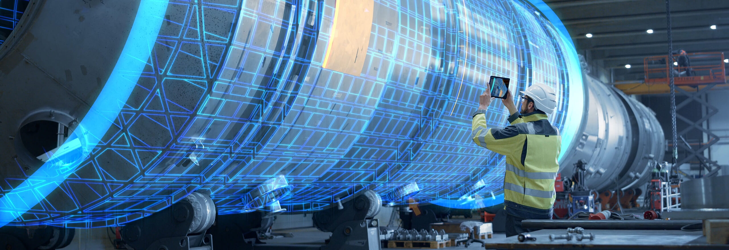 Inżynier na hali produkcyjnej przeprowadza kontrolę turbiny, trzymając w ręce tablet.