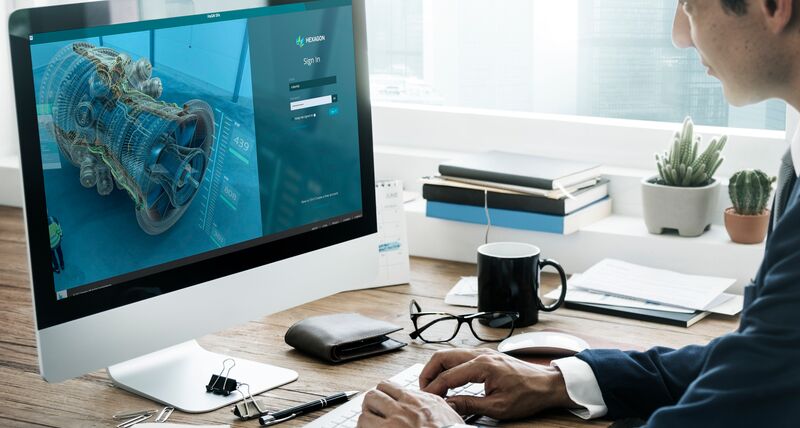 Ingeniero frente a un escritorio mirando el monitor de un ordenador con un aeromotor al lado izquierdo. De lado derecho se encuentra el incio de sesión en la pantalla del software Assessment Management de Hexagon