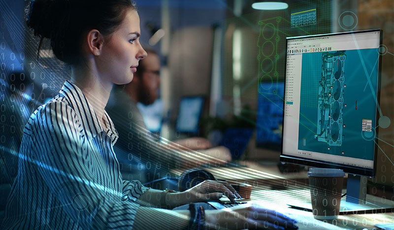 A lady at a computer using PC-DMIS metrology software with a completed inspection of an engine block on screen. There is a blue hue coming from the left side of the image.