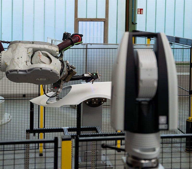 Laser tracker monitoring a robotic arm inspecting an automotive component in a factory, enabling precise automated measurement and alignment.