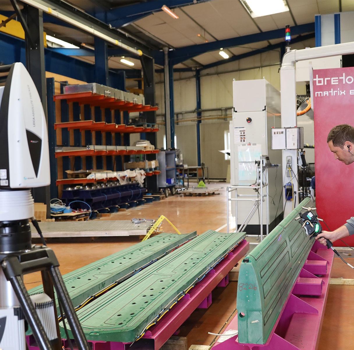 Technician uses a laser tracker and  handheld 3D scanner to inspect long moulded parts in an industrial workshop.