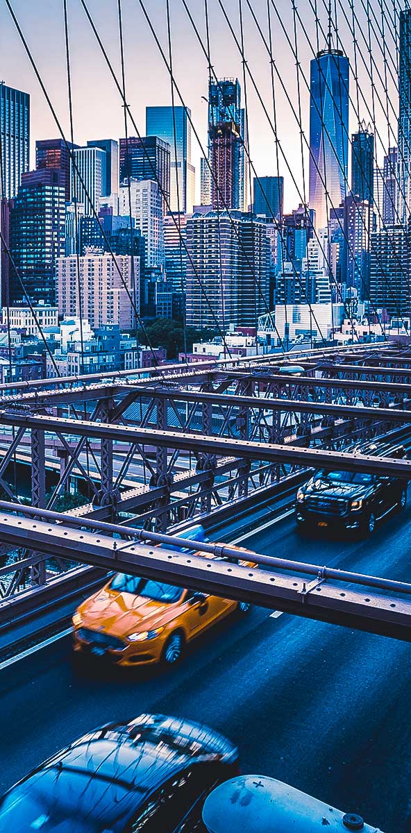 Uma imagem de carros atravessando uma ponte, com uma paisagem urbana ao fundo