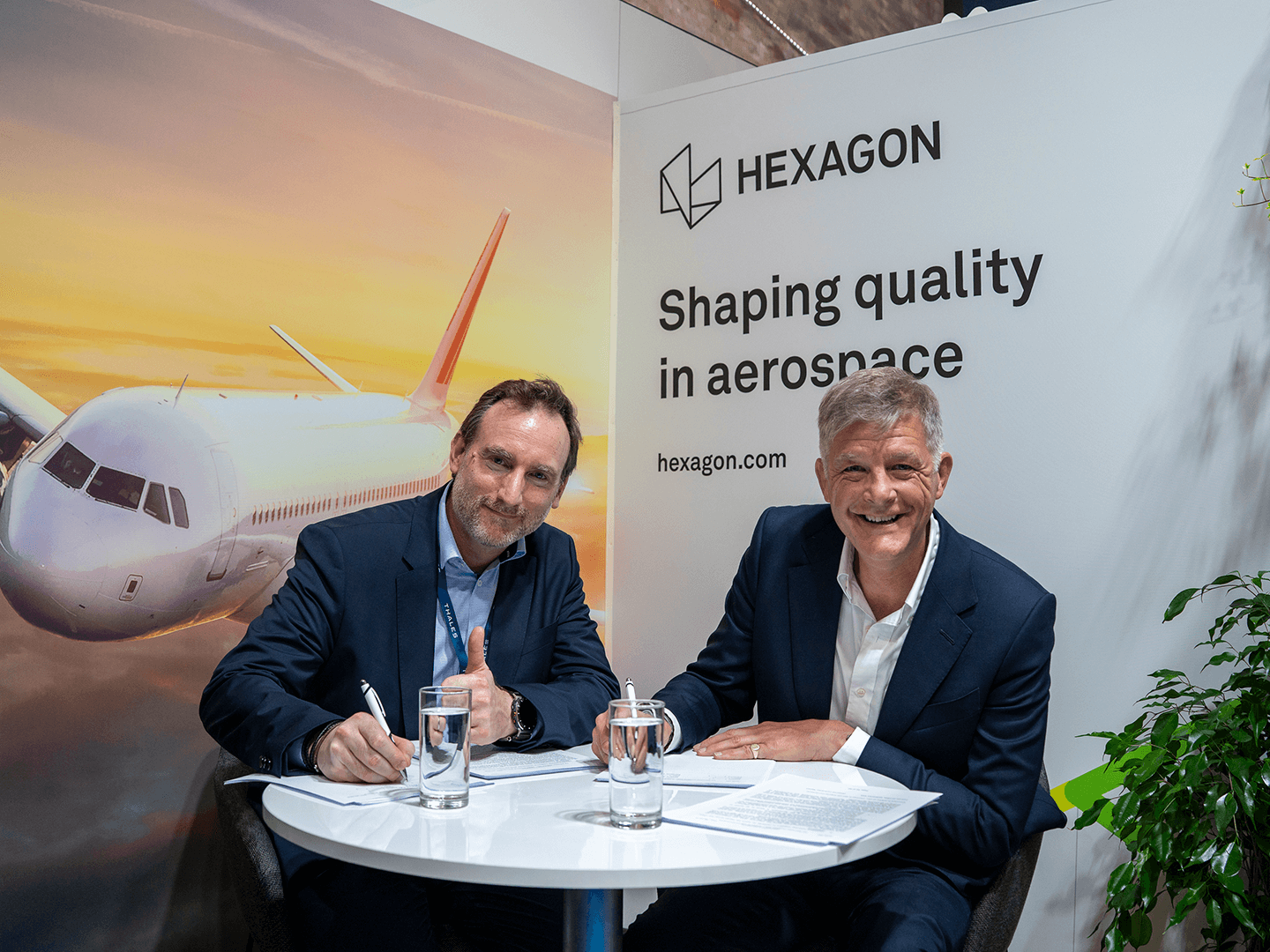 Didier Perrigault and Stephen Chadwick discuss at Paris Air Show 2025, Hexagon's aerospace display behind them.