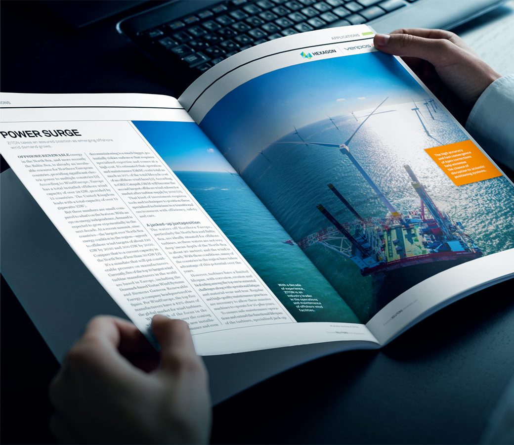 A person at a desk near a keyboard reads Hexagon’s 2023 Velocity magazine article, Power Surge, about positioning offshore wind farms.